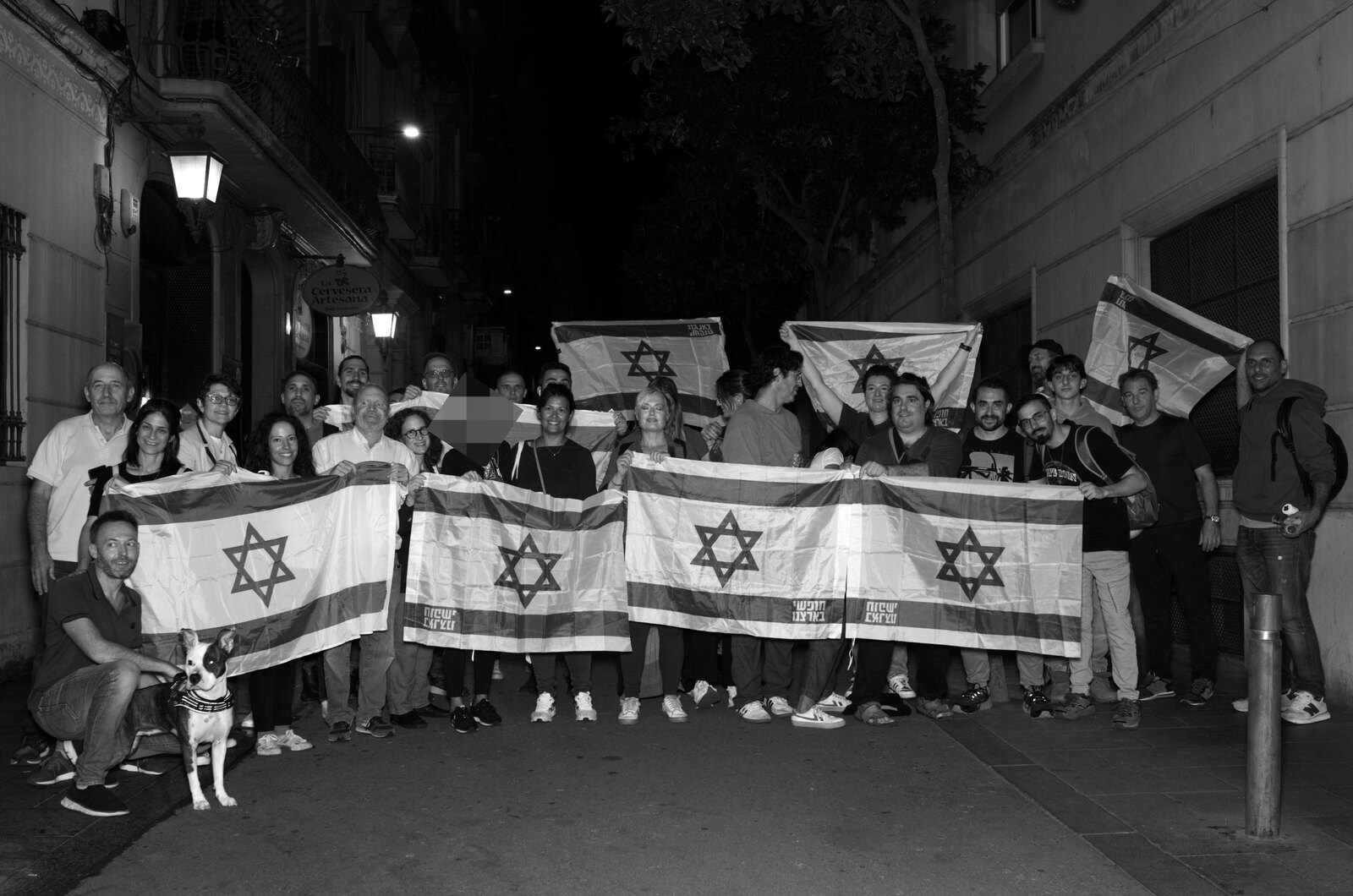 Grupo de participantes con banderas en una calle, de noche.