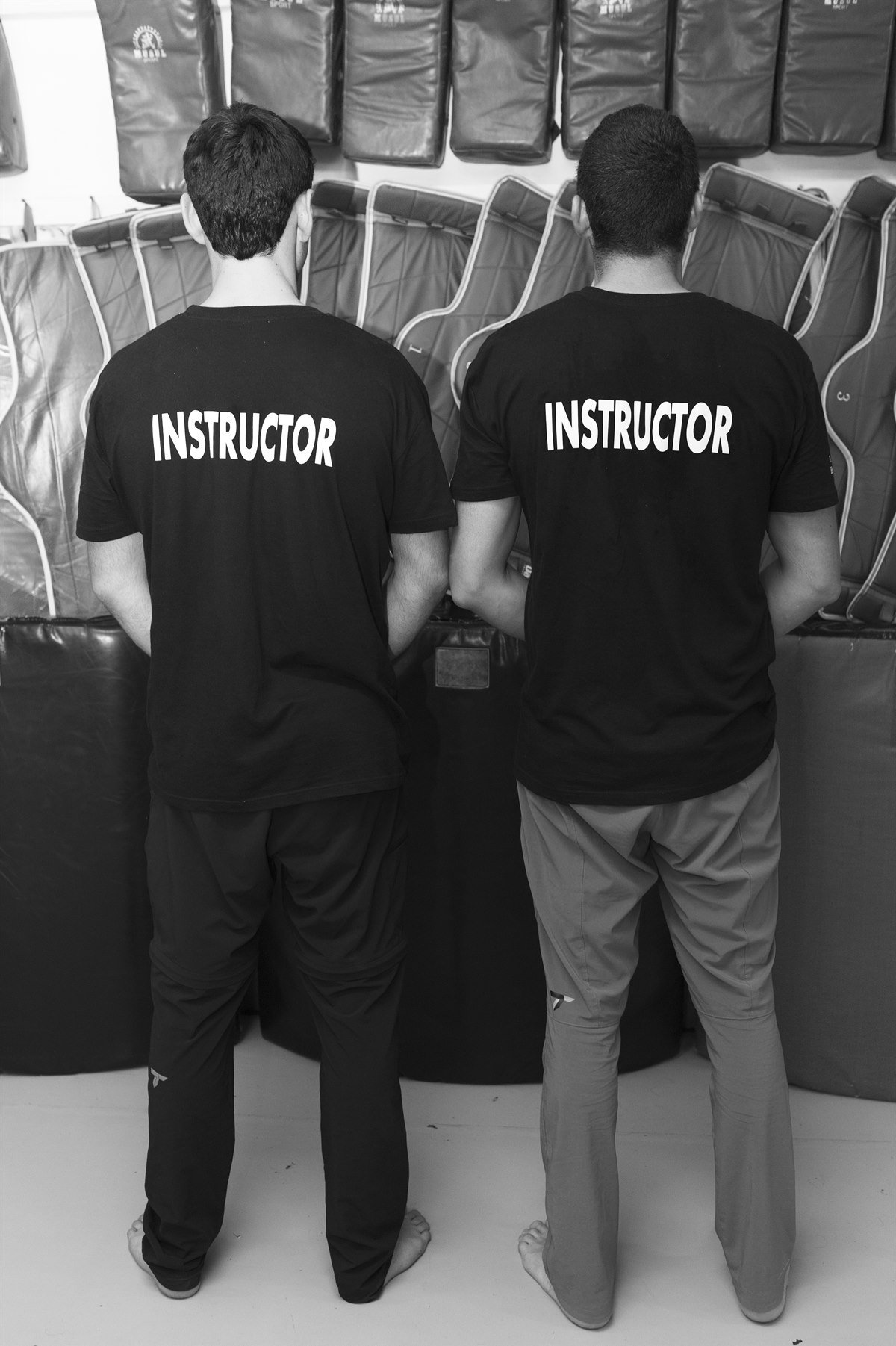 Dos instructores de defensa personal, de espaldas, con camisetas identificativas.