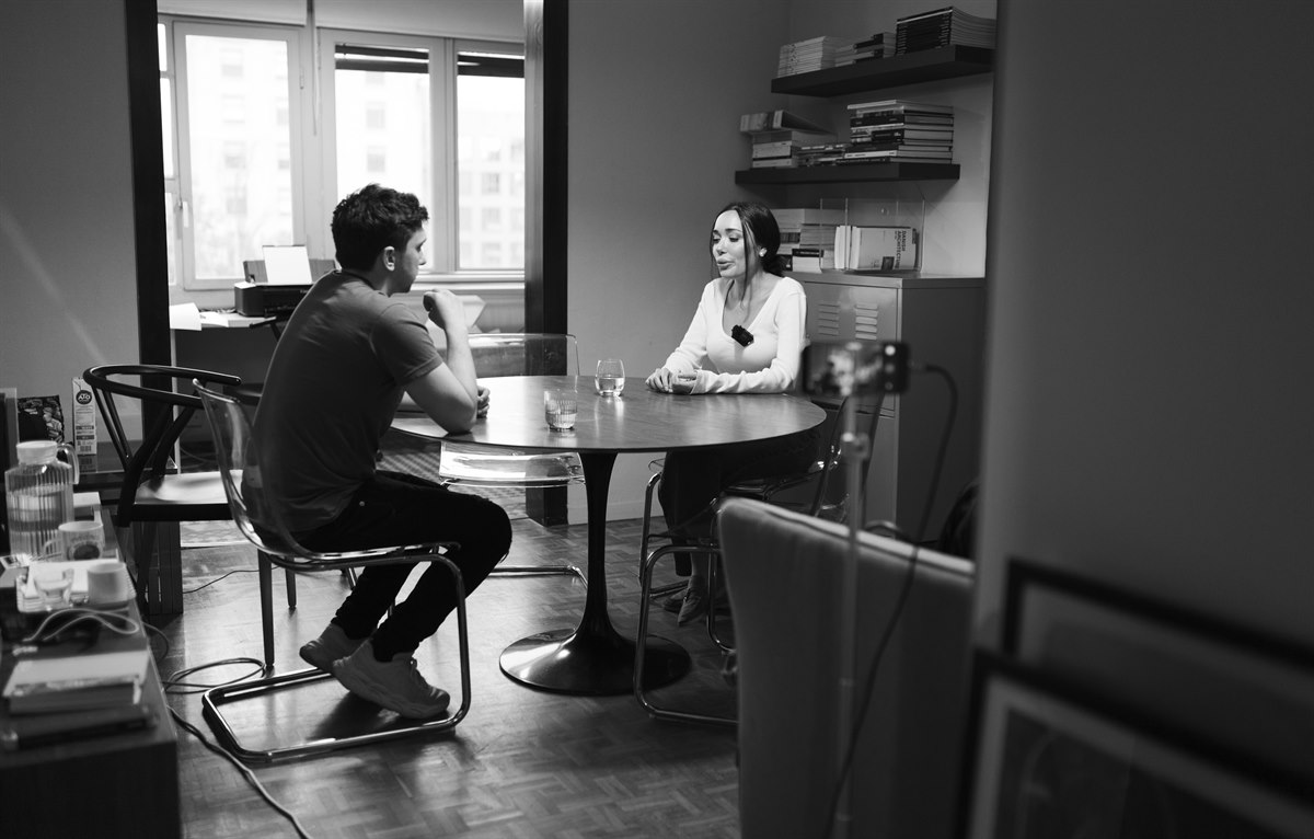 Dos personas conversan sentadas a una mesa durante una grabación.