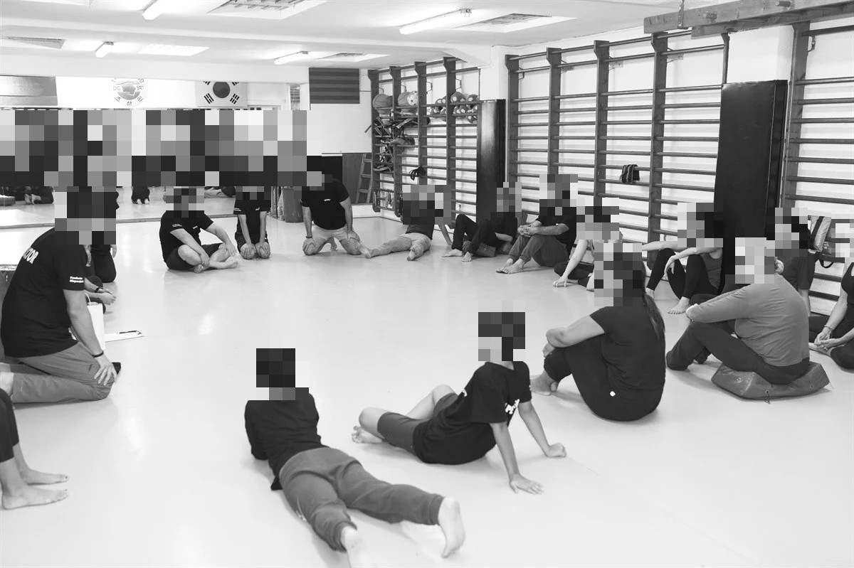 Grupo sentado en el suelo de una sala durante una sesión de defensa personal.